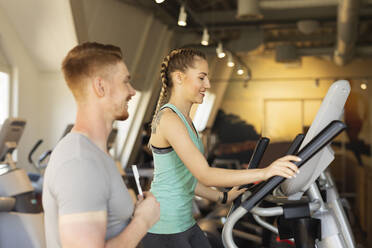 Junge Frau trainiert auf einem Stepper im Fitnessstudio mit Personal Trainer - SEBF00134