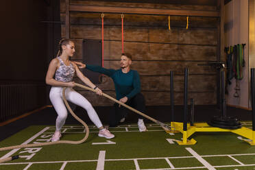 Junge Frau trainiert in einem Fitnessstudio mit einem persönlichen Trainer, der ein Seil zieht - SEBF00141