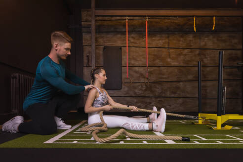 Junge Frau trainiert in einem Fitnessstudio mit einem persönlichen Trainer, der ein Seil zieht - SEBF00143