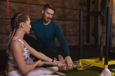 Junge Frau trainiert in einem Fitnessstudio mit einem persönlichen Trainer, der ein Seil zieht - SEBF00144