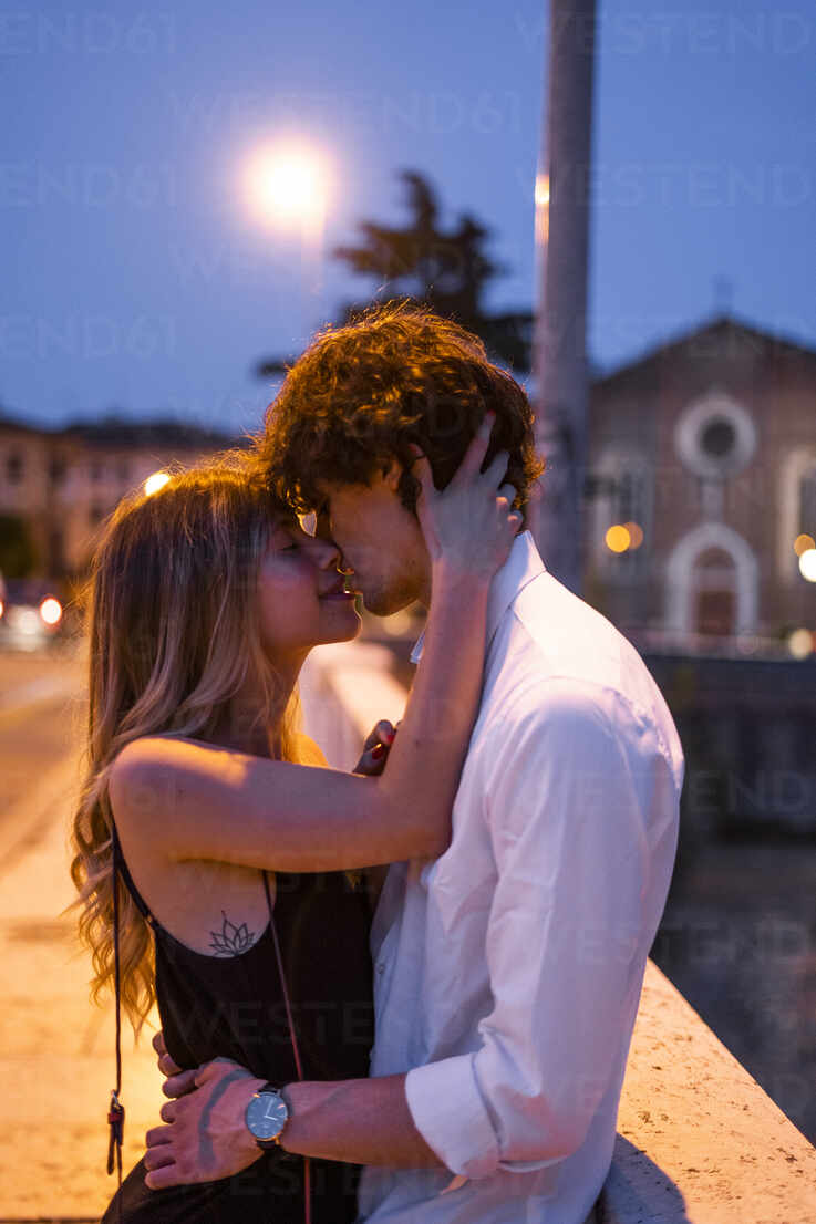 Affectionate young couple kissing inon a bridge at night, Verona