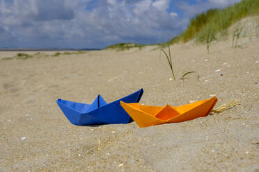 Blue and orange paper boat in the sand at the beach - LBF02653