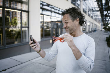 Portrait of mature man with horn and smartphone - KNSF06123