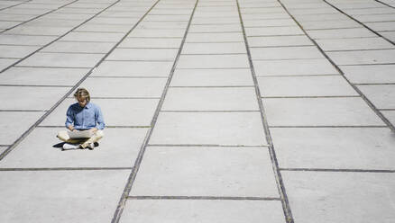 Young man sitting on a square using laptop - KNSF06141