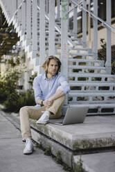 Young man sitting at stairs with laptop - KNSF06152