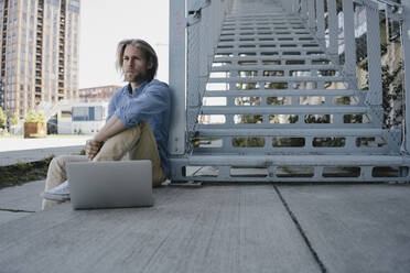 Young man sitting at stairs with laptop - KNSF06171