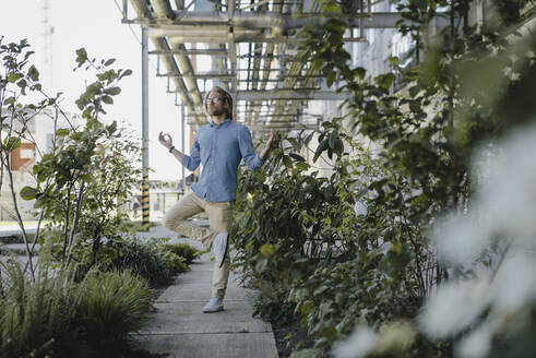 Young man meditating on pavement surrounded by plants - KNSF06174