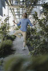 Junger Mann meditiert auf dem Bürgersteig, umgeben von Pflanzen - KNSF06175