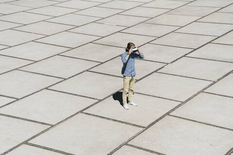 Junger Mann mit VR-Brille steht auf einem Platz, lizenzfreies Stockfoto