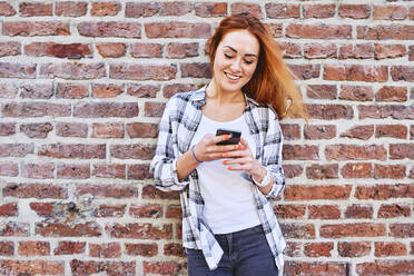 Junge Frau lehnt sich in der Stadt an eine Mauer, während sie ihr Smartphone benutzt - BSZF01315