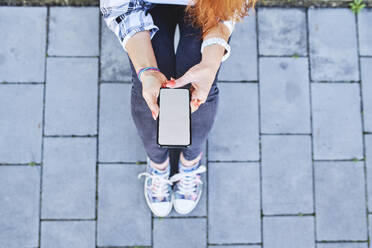 Draufsicht auf eine Frau, die im Freien sitzend ein Smartphone benutzt - BSZF01328