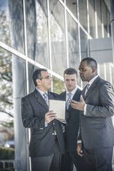 Businessmen using digital tablet outside office - BLEF13530