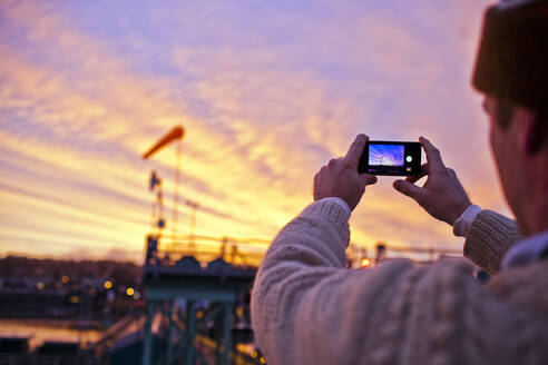 Mann, der den Sonnenuntergang über einer Brücke fotografiert - BLEF13637