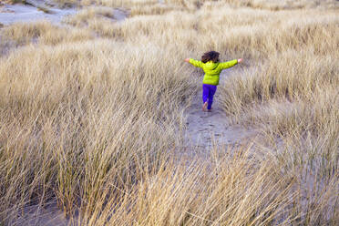 Kaukasisches Mädchen läuft in grasbewachsener Sanddüne - BLEF13642