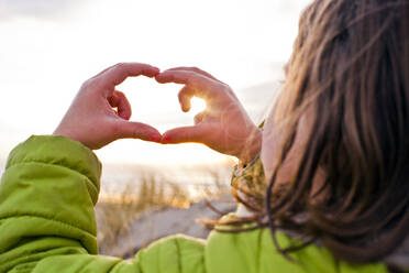 Caucasian girl admiring sunset through hands - BLEF13643