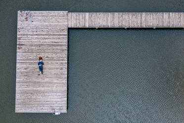 Luftaufnahme einer jungen Triathletin, die auf einem Steg an einem See liegt - STSF02176