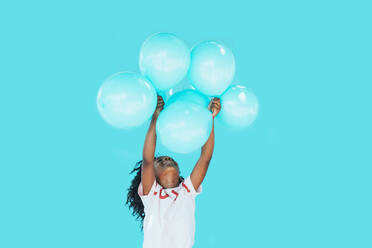 Little girl In front of a blue wall, holding balloons - JCMF00086