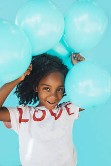 Little girl In front of a blue wall, holding balloons - JCMF00087
