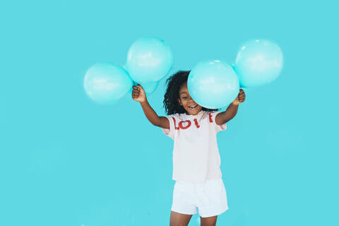 Little girl In front of a blue wall, holding balloons stock photo