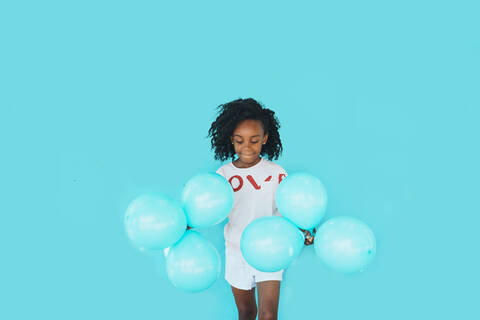 Little girl In front of a blue wall, holding balloons stock photo