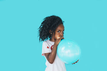 Little girl In front of a blue wall, blowing up balloon - JCMF00092