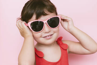 Portrait of smiling little girl wearing sunglasses against pink background - GEMF03035