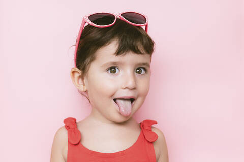 Happy little girl with funny face and tongue out on pink background, lizenzfreies Stockfoto