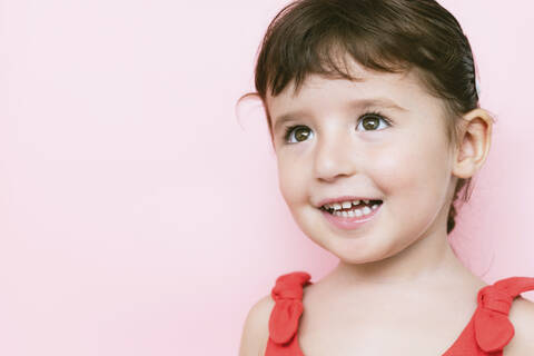 Portrait of smiling little girl in front of pink background looking up stock photo