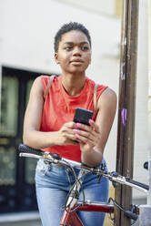 Portrait of young woman leaning on handle bar of bicycle looking at distance - JSMF01207