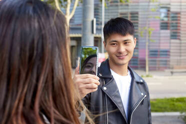 Lächelnder junger Mann, der ein Handyfoto von einer Frau in Barcelona, Spanien, macht - GEMF03051