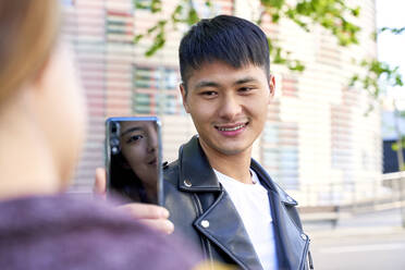 Smiling young man taking a cell phone picture of woman in Barcelona, Spain - GEMF03052