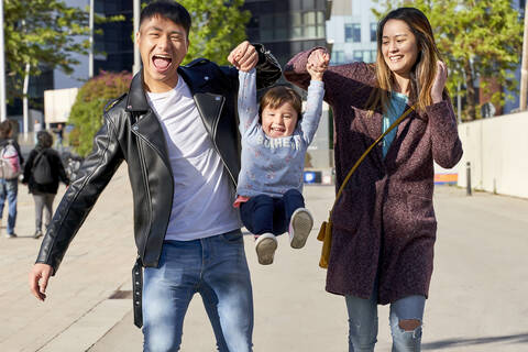 Happy parents holding hands of little girl while jumping, Barcelona, Spain stock photo