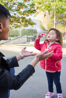 Vater und kleine Tochter spielen mit Seifenblasen im Freien - GEMF03092