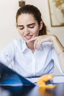 Smiling female student learning at desk at home - LJF00586