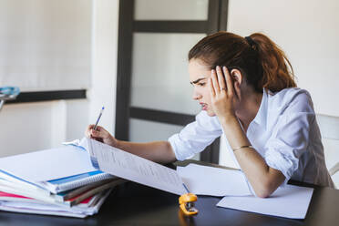 Frustrated female student with documents at desk at home - LJF00588