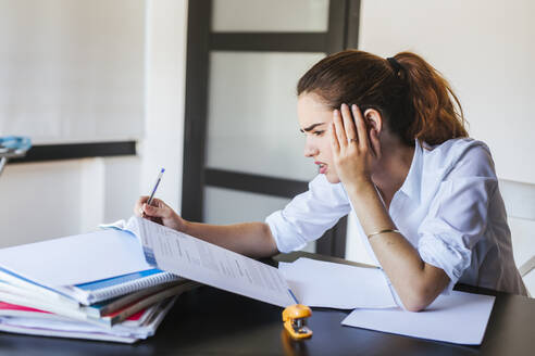 Frustrierte Studentin mit Unterlagen am Schreibtisch zu Hause - LJF00588
