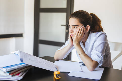Frustrierte Studentin mit Unterlagen am Schreibtisch zu Hause - LJF00590