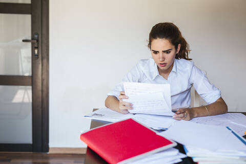 Schockierte Studentin beim Lesen eines Dokuments am Schreibtisch zu Hause, lizenzfreies Stockfoto