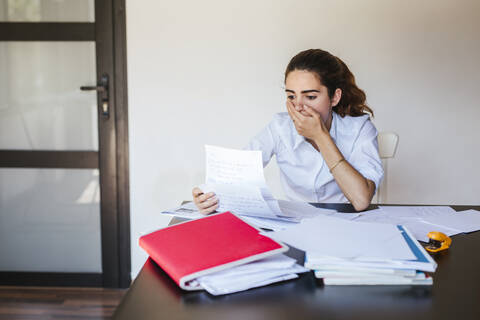 Shocked female student reading document at desk at home stock photo