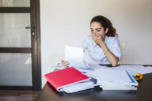 Schockierte Studentin beim Lesen eines Dokuments am Schreibtisch zu Hause - LJF00598