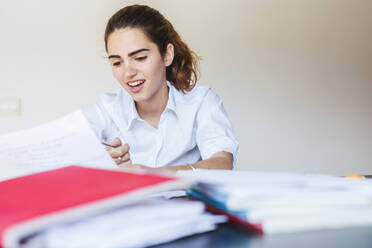 Lächelnde Studentin beim Lesen eines Dokuments am Schreibtisch zu Hause - LJF00602