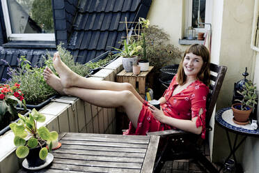 Porträt einer lächelnden jungen Frau, die sich mit einer Tasse Kaffee auf dem Balkon entspannt - FLLF00257