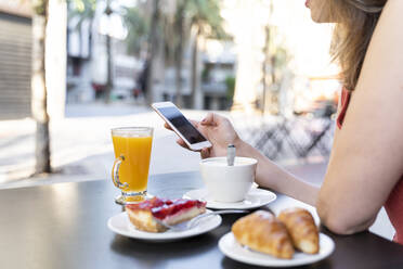 Junge Frau sitzt in einem Straßencafé und benutzt ein Mobiltelefon - AFVF03627