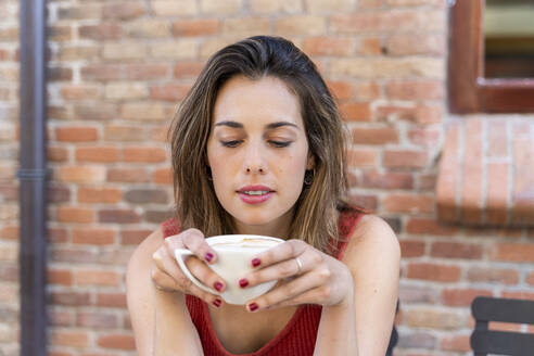 Portrait of young woman sitting at street cafe with cup of coffee - AFVF03628