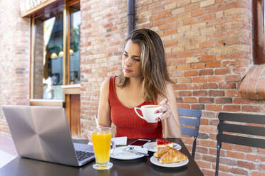 Junge Bloggerin sitzt in einem Straßencafé und schaut auf ihren Laptop - AFVF03643