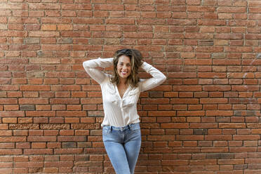 Portrait of smiling woman in front of a brick wall, hands in hair - AFVF03652