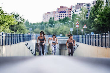 Three sporty young women running on a street - OCMF00547