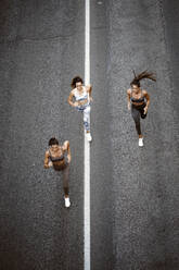 Top view of three sporty young women running on a street - OCMF00549
