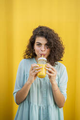 Porträt einer Frau, die Saft trinkt, gelber Hintergrund - AFVF03662