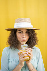 Portrait of woman with straw hat, drinking juice, yellow background - AFVF03663